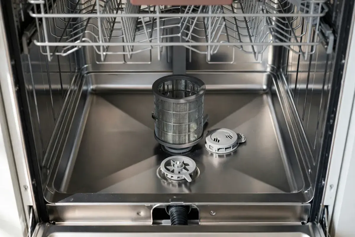 Open dishwasher tub with the lower rack pulled out, showing the filter and spray arm base